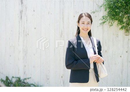 白い塀の前にいるスーツの女性 白い塀の前にいるスーツの女性 128254442