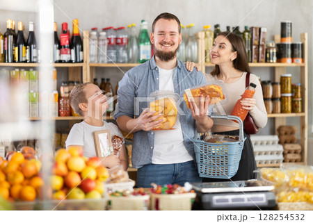 Family with various products in hands continuing shopping in grocery department of supermarket 128254532
