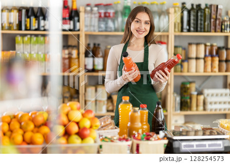 Young woman seller offers juices in grocery store Young woman seller offers juices in grocery store 128254573
