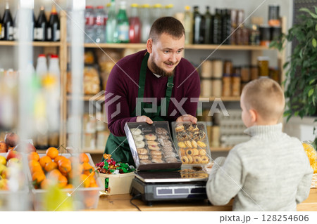 Friendly seller offers cookies to little customer in grocery store Friendly seller offers cookies to little customer in grocery store 128254606