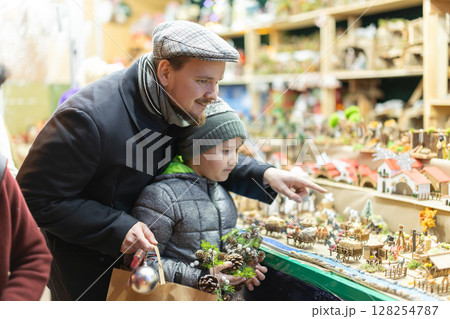 Dad and son standing near counter at Christmas market fair, choosing figurines for nativity scene 128254787