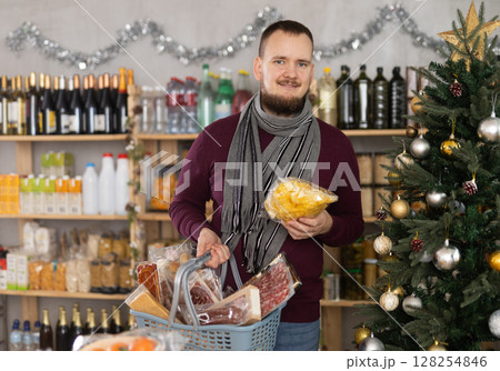 Middle-aged guy choosing chips in a Christmas-decorated store Middle-aged guy choosing chips in a Christmas-decorated store 128254846