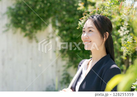 白い塀の前にいるスーツの女性 128255359