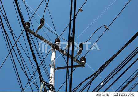 Tangled network of overhead power lines and cables against a clear blue sky. Tangled network of overhead power lines and cables against a clear blue sky. 128255679