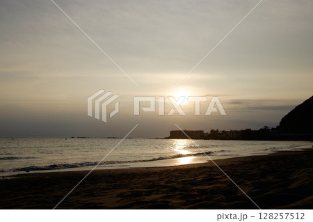 夕日で黄金色に染まった初夏の穏やかな海と岬と砂浜 128257512