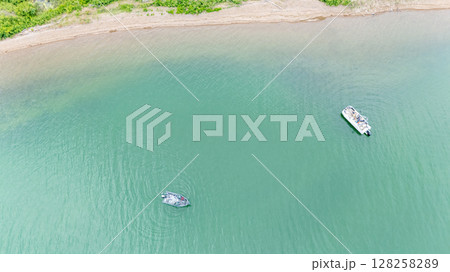 overhead view of a boat and pontoon fishing along the shore of a river. 128258289