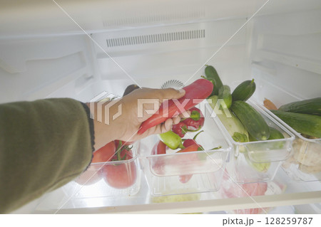 Fresh vegetables in refrigerator with hand selecting peppers Fresh vegetables in refrigerator with hand selecting peppers 128259787