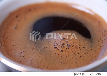 Dark, rich coffee brew in a cup with foamy surface 128259895