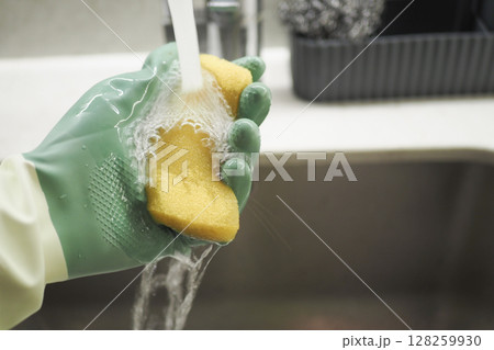 Washing a sponge under running water in the kitchen sink Washing a sponge under running water in the kitchen sink 128259930