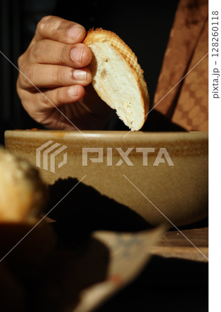 Enjoying warm bread with savory dip in cozy setting Enjoying warm bread with savory dip in cozy setting 128260118