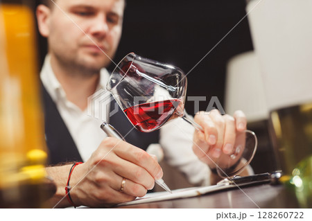Skilled male sommelier looks carefully at drink in stem glass. 128260722