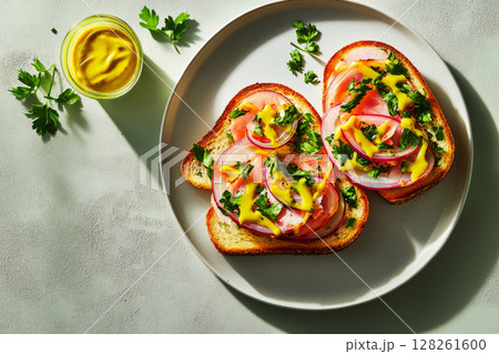 A delicious breakfast featuring toasted bread layered with slices of tomato, onion, and herbs, drizzled with mustard on a simple plate. Perfect for a healthy start to the day 128261600
