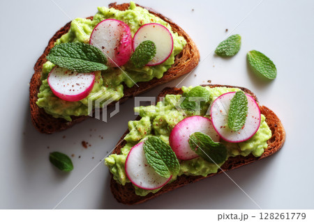 Brightly colored breakfast includes slices of toasted bread layered with creamy avocado, garnished with fresh radishes and mint leaves, perfect for a sunny morning Brightly colored breakfast includes slices of toasted bread layered with creamy avocado, garnished with fresh radishes and mint leaves, perfect for a sunny morning 128261779