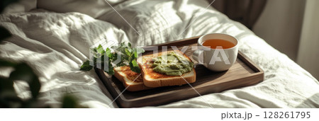 Sliced bread topped with vibrant avocado and diced tomatoes sits on a wooden tray alongside fresh mint leaves and a cup of tea, creating the perfect breakfast in a relaxed setting, banner 128261795
