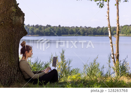 A woman works outdoors by a serene lakeside, enjoying natures beauty and tranquility A woman works outdoors by a serene lakeside, enjoying natures beauty and tranquility 128263768