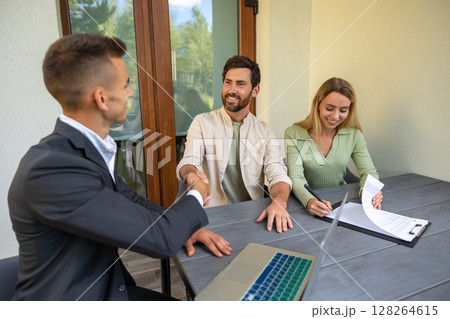 Real estate agent finalizing property contract with couple at outdoor table with laptop and paperwork Real estate agent finalizing property contract with couple at outdoor table with laptop and paperwork 128264615