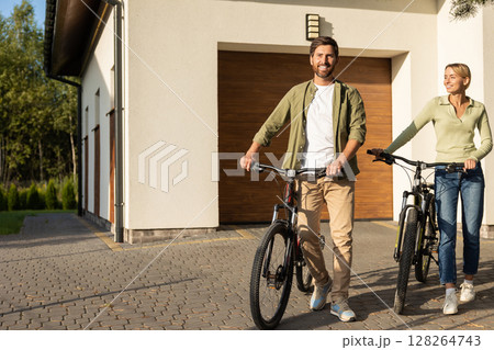 Couple preparing for bike ride outside modern house with garage 128264743