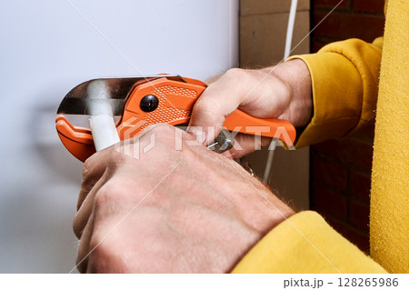 Ratchet pipe cutter slices multilayer pipe as hands operate tool during pipe cutting process for plumbing work. 128265986