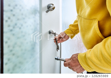 Tightening connection nut with open end wrench, plumber attaches new shower hose to water outlet fitting on panel inside shower cabin. Tightening connection nut with open end wrench, plumber attaches new shower hose to water outlet fitting on panel inside shower cabin. 128265989