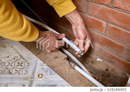 Plumber places compression fitting nut onto end of multilayer pipe along brick wall for connecting water supply lines in residential plumbing system. 128266001