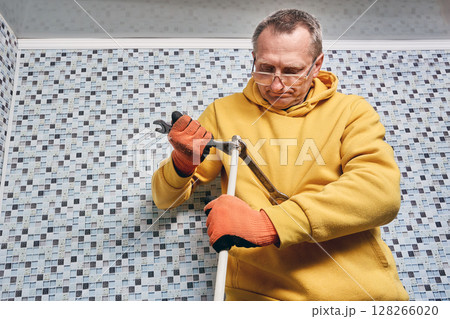 Installation of compression fitting on composite pipe is performed by plumber tightening securing nut with two wrenches to connect plumbing lines. 128266020