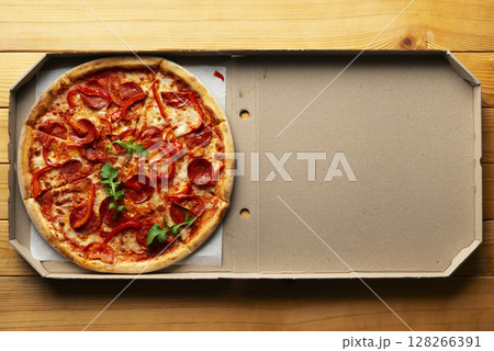 Pepperoni pizza with bell peppers and arugula in open carton box on natural wooden kitchen table flat lay with copy-space Pepperoni pizza with bell peppers and arugula in open carton box on natural wooden kitchen table flat lay with copy-space 128266391