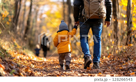 Father and child walking hand in hand through a serene fall forest trail 128266543