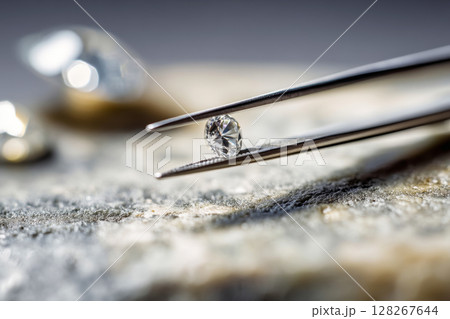 Diamond gemstone held by metal tweezers, close up 128267644