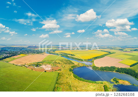 Sunny day in the village. Rural landscape in daylight. Aerial view of a meandering river, cultivated fields, and a beautiful cloudy sky. 128268108