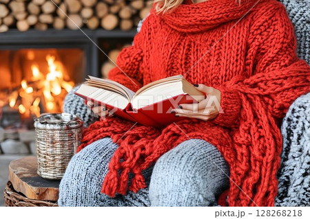 Cozy Comfort: Woman reading a book by the fireplace in winter season 128268218