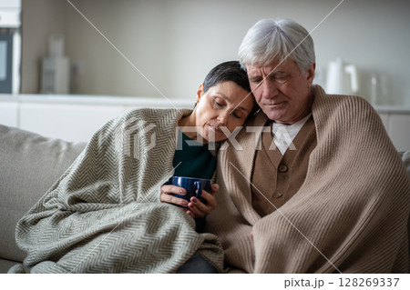 Weakened older pair wrapped together drinking herbal infusion while battling fever and exhaustion Weakened older pair wrapped together drinking herbal infusion while battling fever and exhaustion 128269337