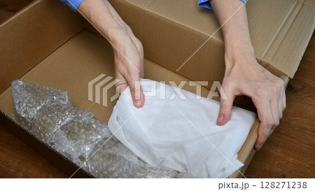 Packing up fragile tableware wrapped in plastic inside cardboard box Packing up fragile tableware wrapped in plastic inside cardboard box 128271238