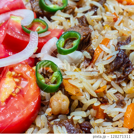 A rice dish with meat, garnished with a salad of chopped tomatoes, onions and hot green chili peppers. The photo is suitable for both the restaurant business and any food related design 128271311