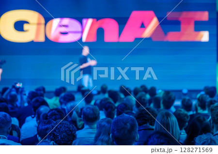 Speaker addressing large audience at blue tech conference with GenAI theme 128271569