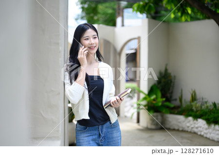 Confident young woman smiling while talking on the phone outside a stylish modern cafe Confident young woman smiling while talking on the phone outside a stylish modern cafe 128271610