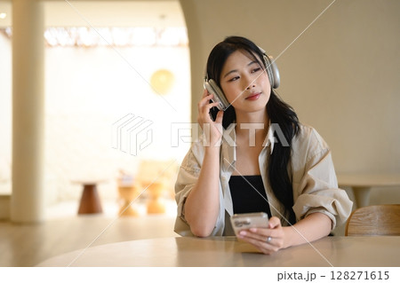 Relaxed woman enjoying music and browsing her phone at a round table Relaxed woman enjoying music and browsing her phone at a round table 128271615