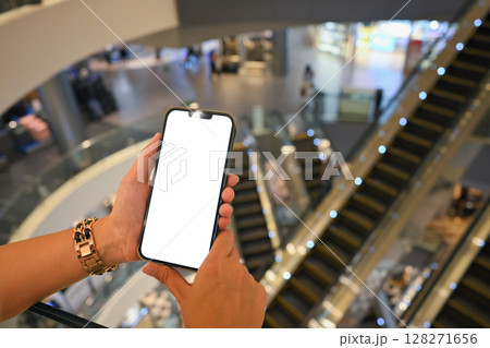 Close up of female hands using smartphone with blank white screen in a modern shopping mall 128271656