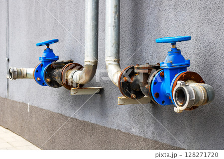 A long row of pipes equipped with blue valves mounted on a wall A long row of pipes equipped with blue valves mounted on a wall 128271720