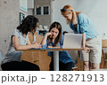 Three female colleagues reviewing meeting notes and feedback in bright office cafeteria 128271913