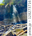 Water flows powerfully over rocks creating mist in bright sunlight. Scenic landscape with vibrant green trees and clear blue sky. Concept of nature exploration, adventure tourism, outdoor photography. 128273716