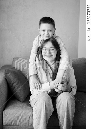Little boy hugging his older sister. Happy siblings smiling to camera. Adorable kids having fun together at home. Black and white image. Little boy hugging his older sister. Happy siblings smiling to camera. Adorable kids having fun together at home. Black and white image. 128273772