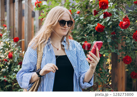 A portrait of a smiling beautiful 30s woman texting with her phone. Summer time. Young female in casual clothing standing outdoor A portrait of a smiling beautiful 30s woman texting with her phone. Summer time. Young female in casual clothing standing outdoor 128273800