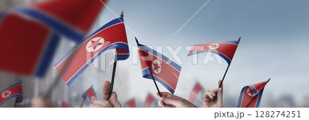 North Korea flags in their hands on a blurred urban background North Korea flags in their hands on a blurred urban background 128274251