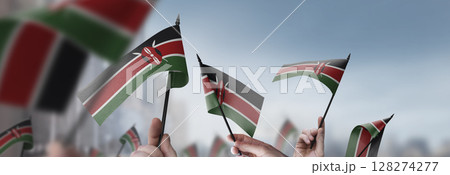 Kenya flags in their hands on a blurred urban background 128274277