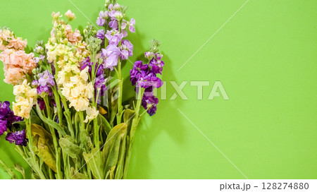Mixed flower stems including soft pinks and purples are positioned on a green surface, ready for wrapping. The vibrant color contrast adds a cheerful tone. 128274880