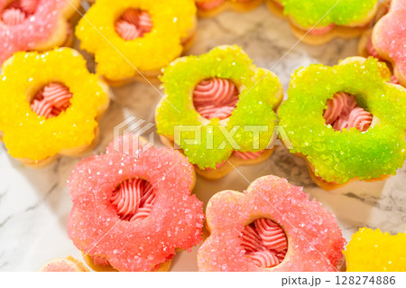 An assortment of Easter cookie sandwiches decorated with pink, green, and yellow sanding sugar, filled with raspberry buttercream. These festive cookies are part of the Easter Cookie Sandwich with 128274886
