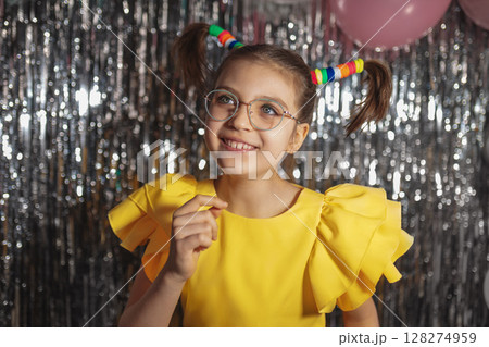 Happy funny girl in glasses and yellow holiday blouse with ponytails hairstyle on festive background Happy funny girl in glasses and yellow holiday blouse with ponytails hairstyle on festive background 128274959