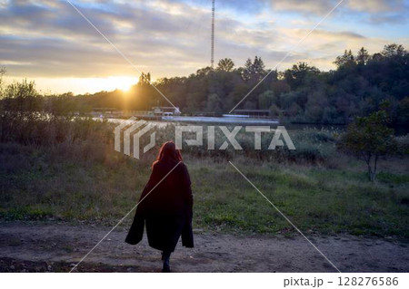 a 15-year-old teenage girl in a black long coat at sunset by the river a 15-year-old teenage girl in a black long coat at sunset by the river 128276586