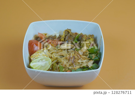 A flavorful Indonesian dish featuring vermicelli, vegetables, and meat, garnished with fried shallots and lime, served in a white bowl. 128276711