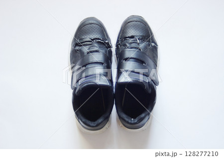 白い紙の上に揃えて置いた、アッパーの部分が破けた合皮のマジックテープ留めスニーカー 128277210